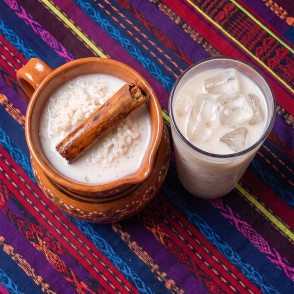 Horchata in a clay mug with a cinnamon stick and a glass of horchata with ice.
