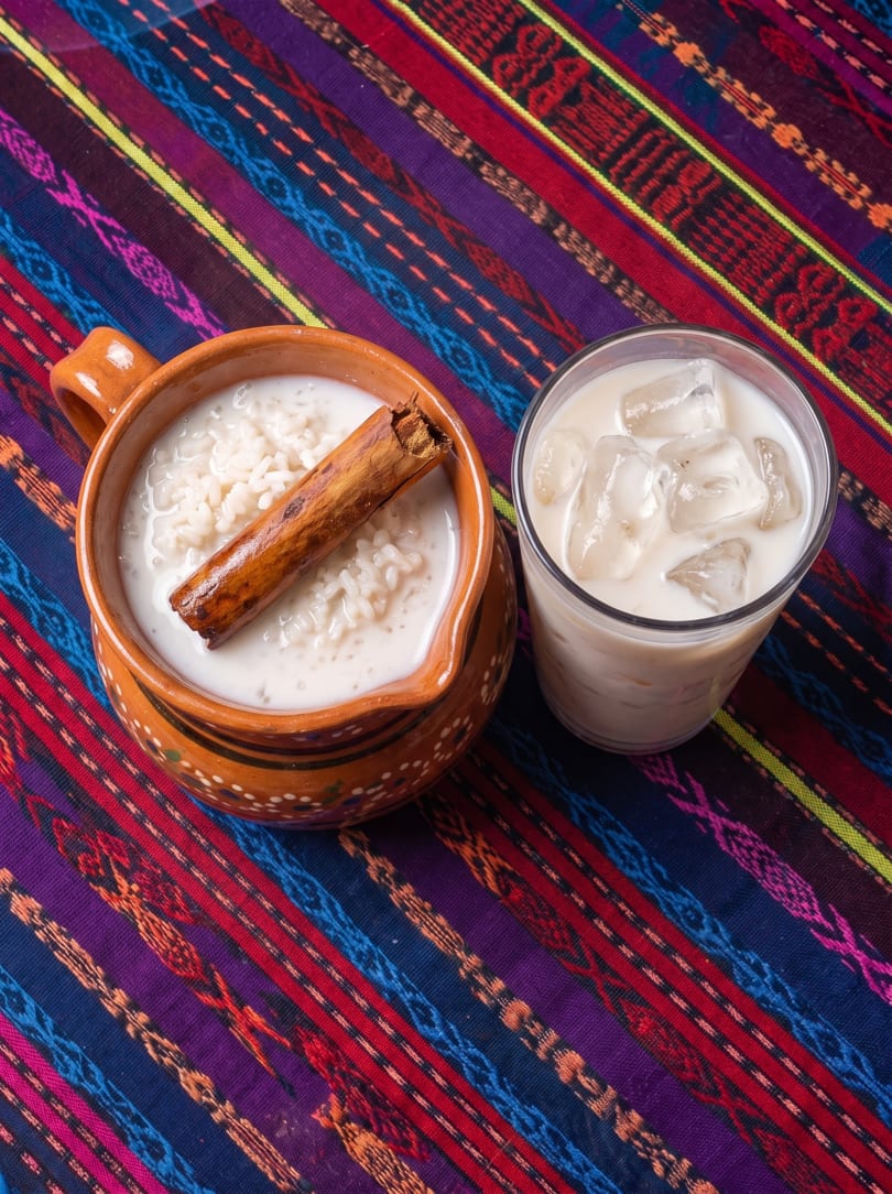Horchata in a clay mug with a cinnamon stick and a glass of horchata with ice.